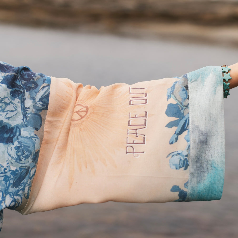 
                  
                    Model wearing our Peace Out Pixie Duster featuring 1800's perfumeur sign with gentle tones of blue & aqua, landscapes, clouds, dove and peace symbols -Market of Stars.
                  
                