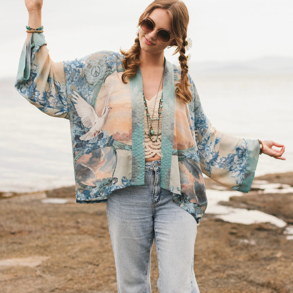 
                  
                    Model wearing our Peace Out Pixie Duster featuring 1800's perfumeur sign with gentle tones of blue & aqua, landscapes, clouds, dove and peace symbols -Market of Stars.
                  
                