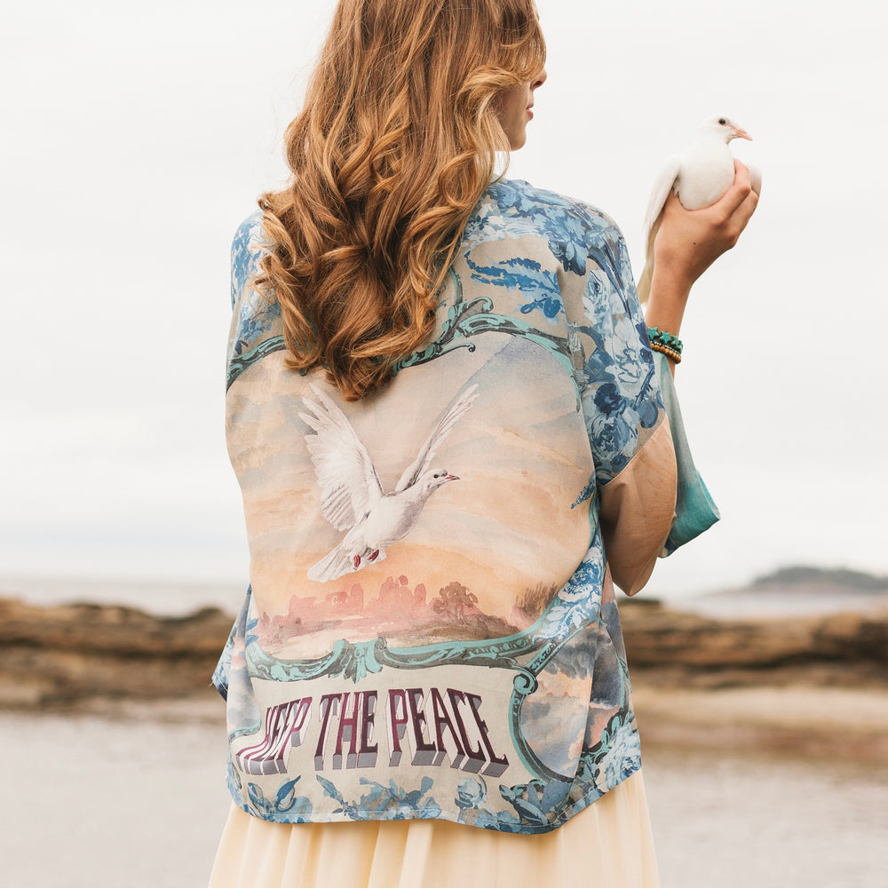 
                  
                    Model wearing our Peace Out Pixie Duster featuring 1800's perfumeur sign with gentle tones of blue & aqua, landscapes, clouds, dove and peace symbols -Market of Stars.
                  
                