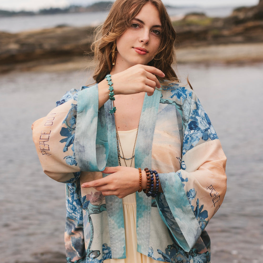 
                  
                    Model wearing our Peace Out Pixie Duster featuring 1800's perfumeur sign with gentle tones of blue & aqua, landscapes, clouds, dove and peace symbols -Market of Stars.
                  
                