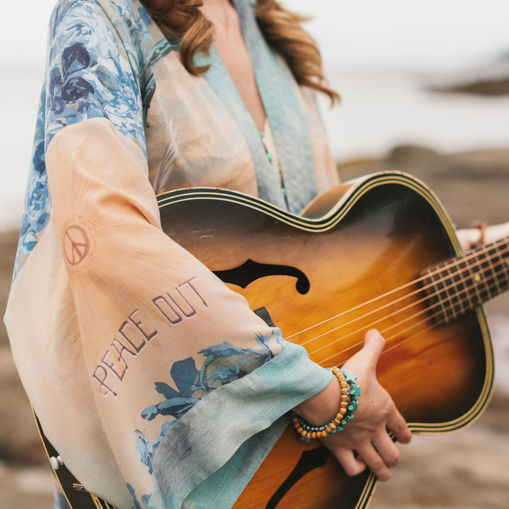
                  
                    Model wearing our Peace Out Pixie Duster featuring 1800's perfumeur sign with gentle tones of blue & aqua, landscapes, clouds, dove and peace symbols -Market of Stars.
                  
                