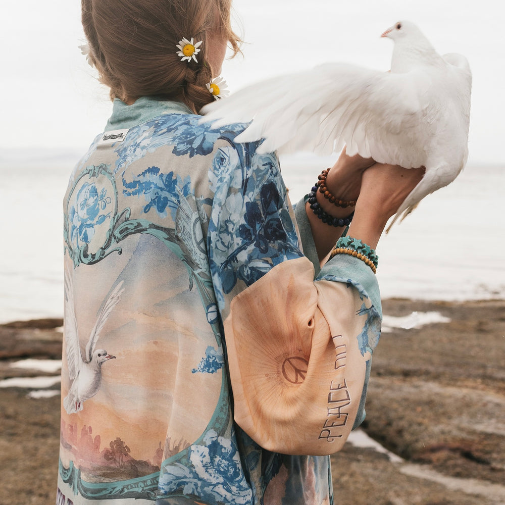 
                  
                    Model wearing our Peace Out Pixie Duster featuring 1800's perfumeur sign with gentle tones of blue & aqua, landscapes, clouds, dove and peace symbols -Market of Stars.
                  
                