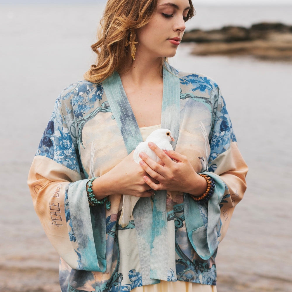 
                  
                    Model wearing our Peace Out Pixie Duster featuring 1800's perfumeur sign with gentle tones of blue & aqua, landscapes, clouds, dove and peace symbols -Market of Stars.
                  
                