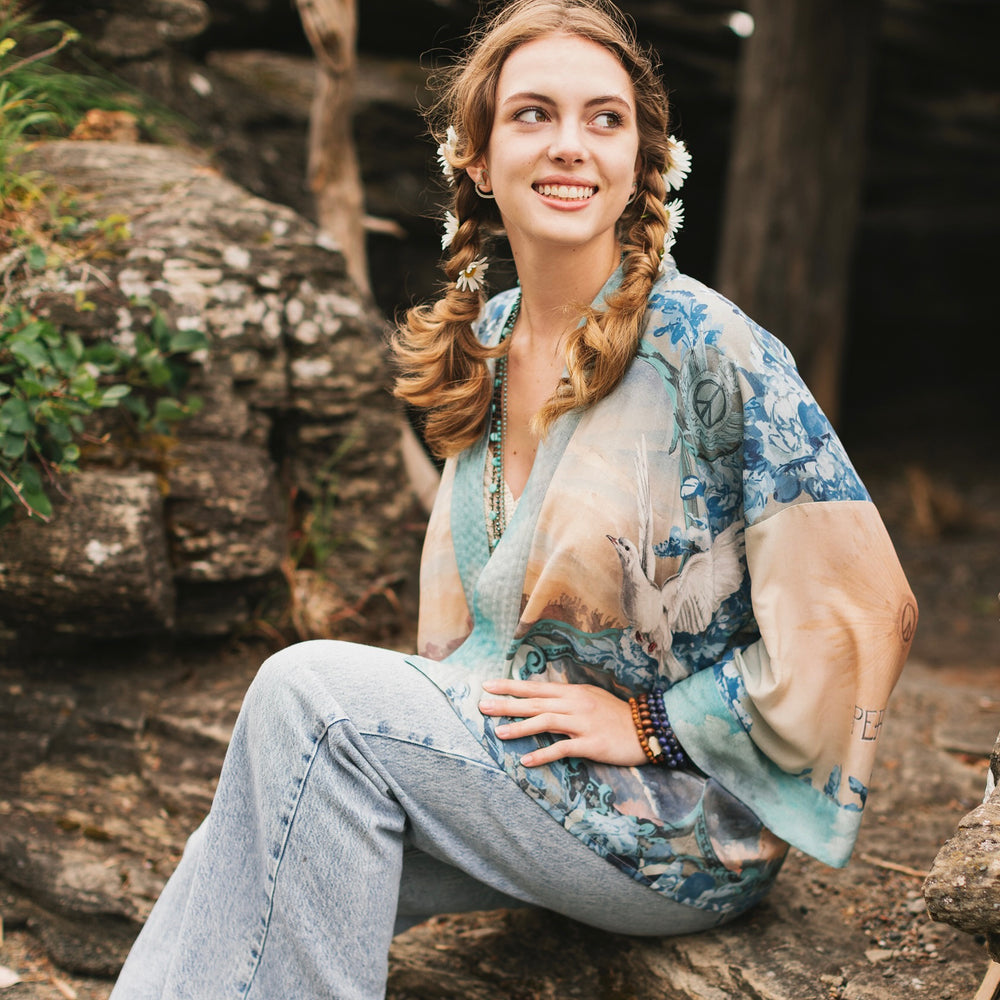 
                  
                    Model wearing our Peace Out Pixie Duster featuring 1800's perfumeur sign with gentle tones of blue & aqua, landscapes, clouds, dove and peace symbols -Market of Stars.
                  
                