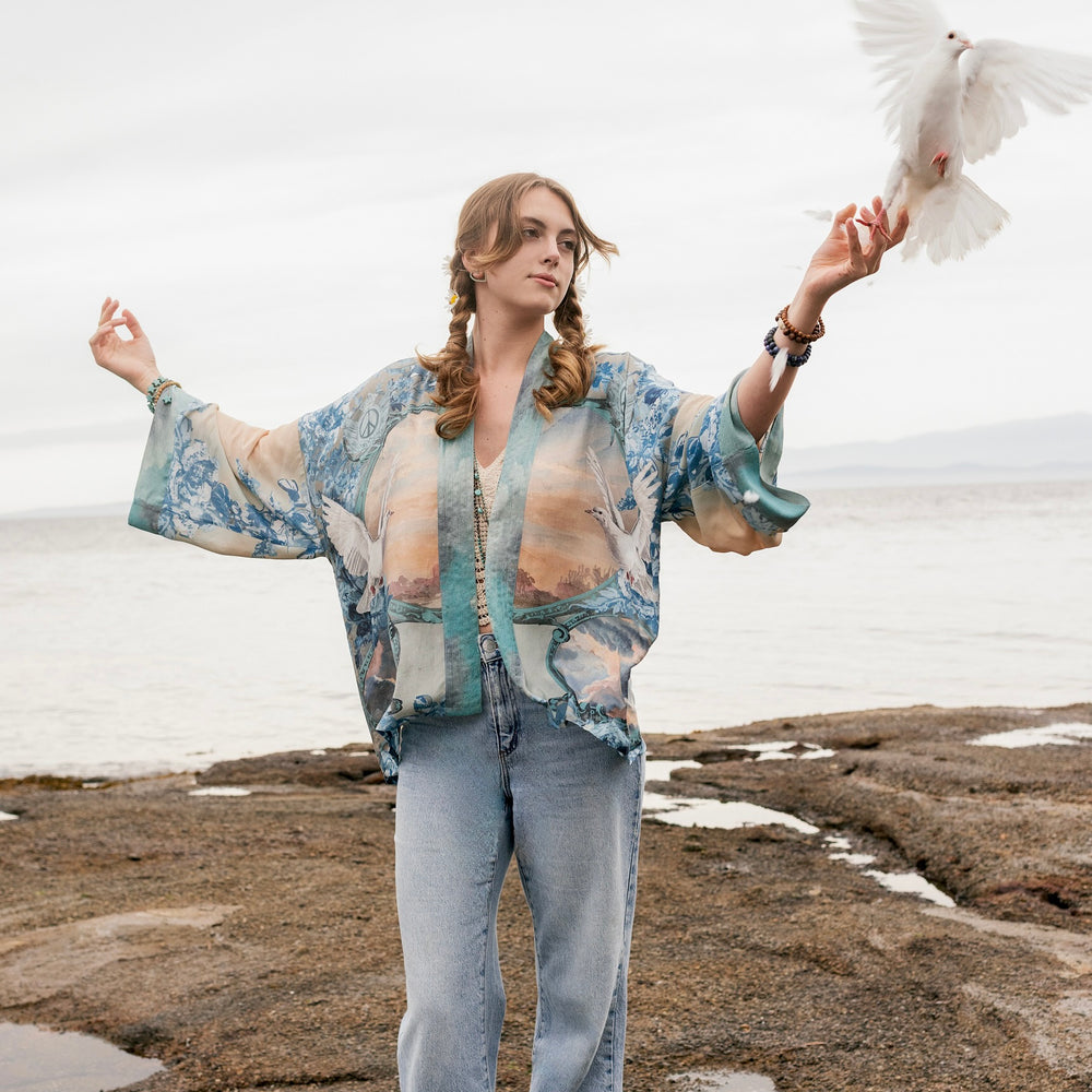 
                  
                    Model wearing our Peace Out Pixie Duster featuring 1800's perfumeur sign with gentle tones of blue & aqua, landscapes, clouds, dove and peace symbols -Market of Stars.
                  
                