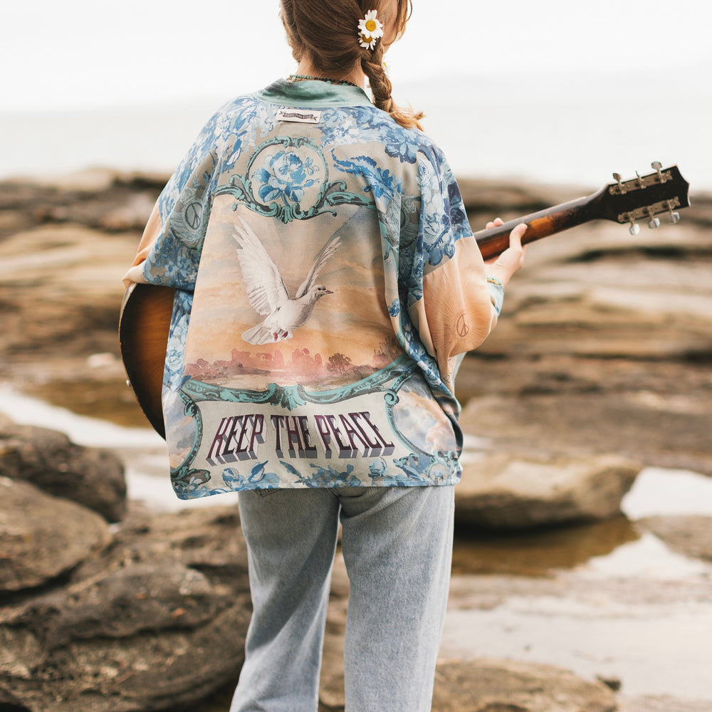 
                  
                    Model wearing our Peace Out Pixie Duster featuring 1800's perfumeur sign with gentle tones of blue & aqua, landscapes, clouds, dove and peace symbols -Market of Stars.
                  
                