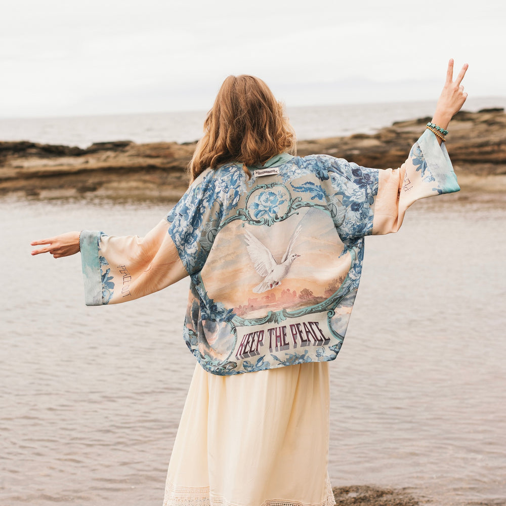 
                  
                    Model wearing our Peace Out Pixie Duster featuring 1800's perfumeur sign with gentle tones of blue & aqua, landscapes, clouds, dove and peace symbols -Market of Stars.
                  
                