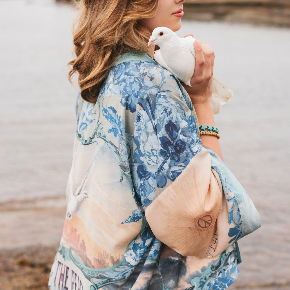 
                  
                    Model wearing our Peace Out Pixie Duster featuring 1800's perfumeur sign with gentle tones of blue & aqua, landscapes, clouds, dove and peace symbols -Market of Stars.
                  
                
