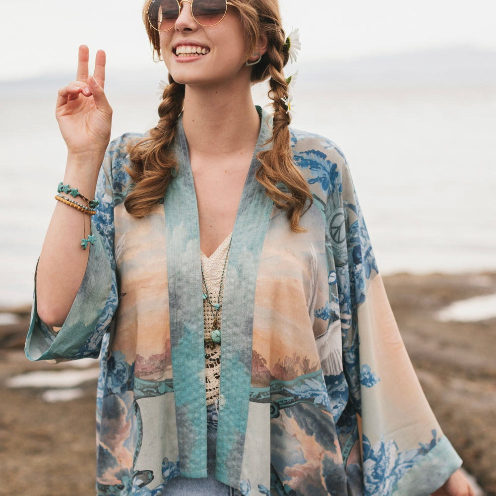 
                  
                    Model wearing our Peace Out Pixie Duster featuring 1800's perfumeur sign with gentle tones of blue & aqua, landscapes, clouds, dove and peace symbols -Market of Stars.
                  
                
