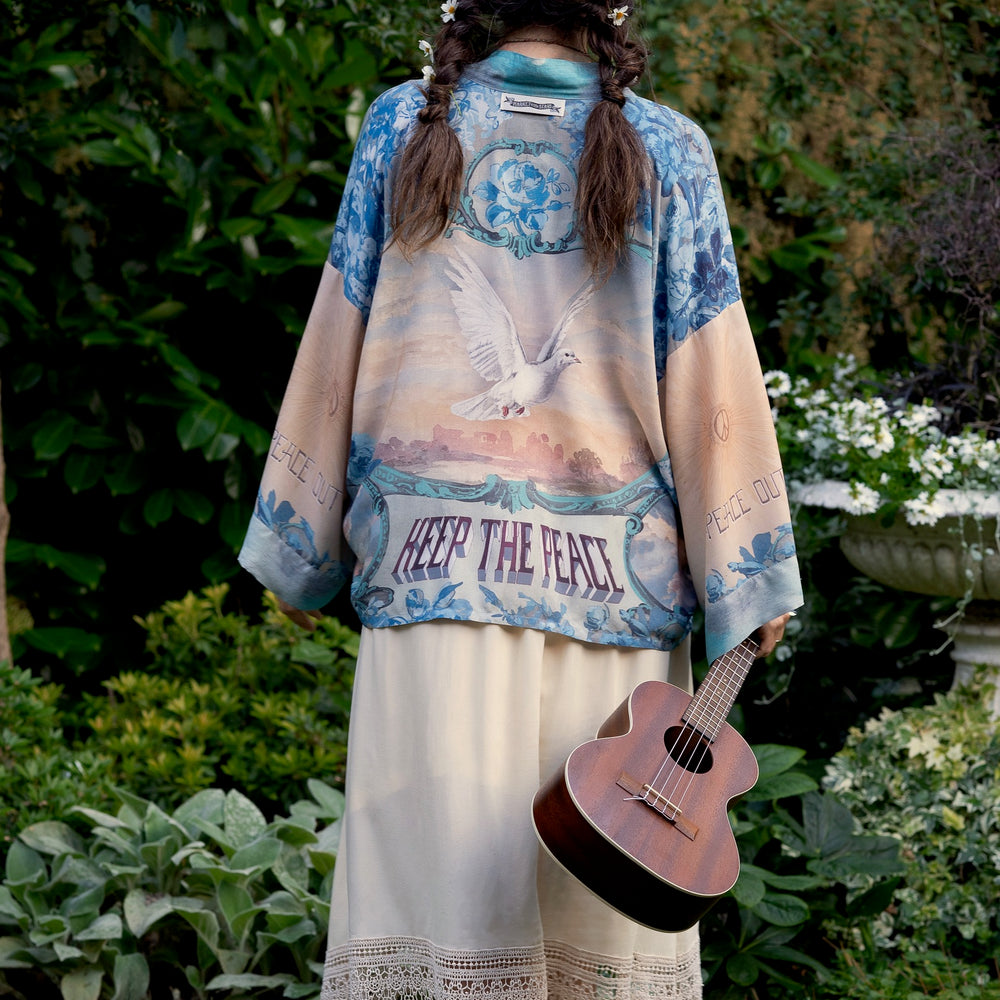 Model wearing our Peace Out Pixie Duster featuring 1800's perfumeur sign with gentle tones of blue & aqua, landscapes, clouds, dove and peace symbols -Market of Stars.