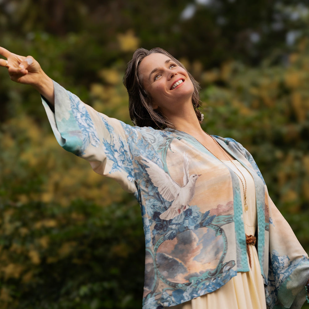 Model wearing our Peace Out Pixie Duster featuring 1800's perfumeur sign with gentle tones of blue & aqua, landscapes, clouds, dove and peace symbols -Market of Stars.