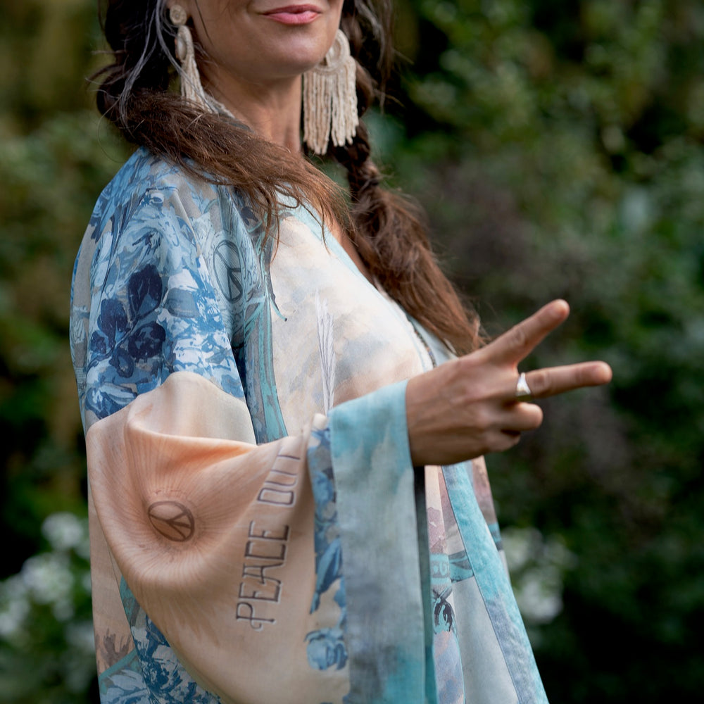 
                  
                    Model wearing our Peace Out Pixie Duster featuring 1800's perfumeur sign with gentle tones of blue & aqua, landscapes, clouds, dove and peace symbols -Market of Stars.
                  
                