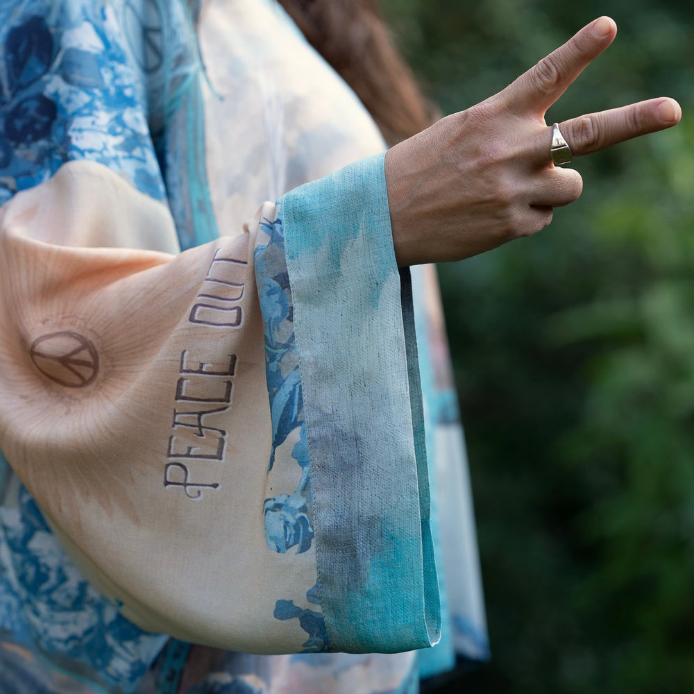 
                  
                    Model wearing our Peace Out Pixie Duster featuring 1800's perfumeur sign with gentle tones of blue & aqua, landscapes, clouds, dove and peace symbols -Market of Stars.
                  
                