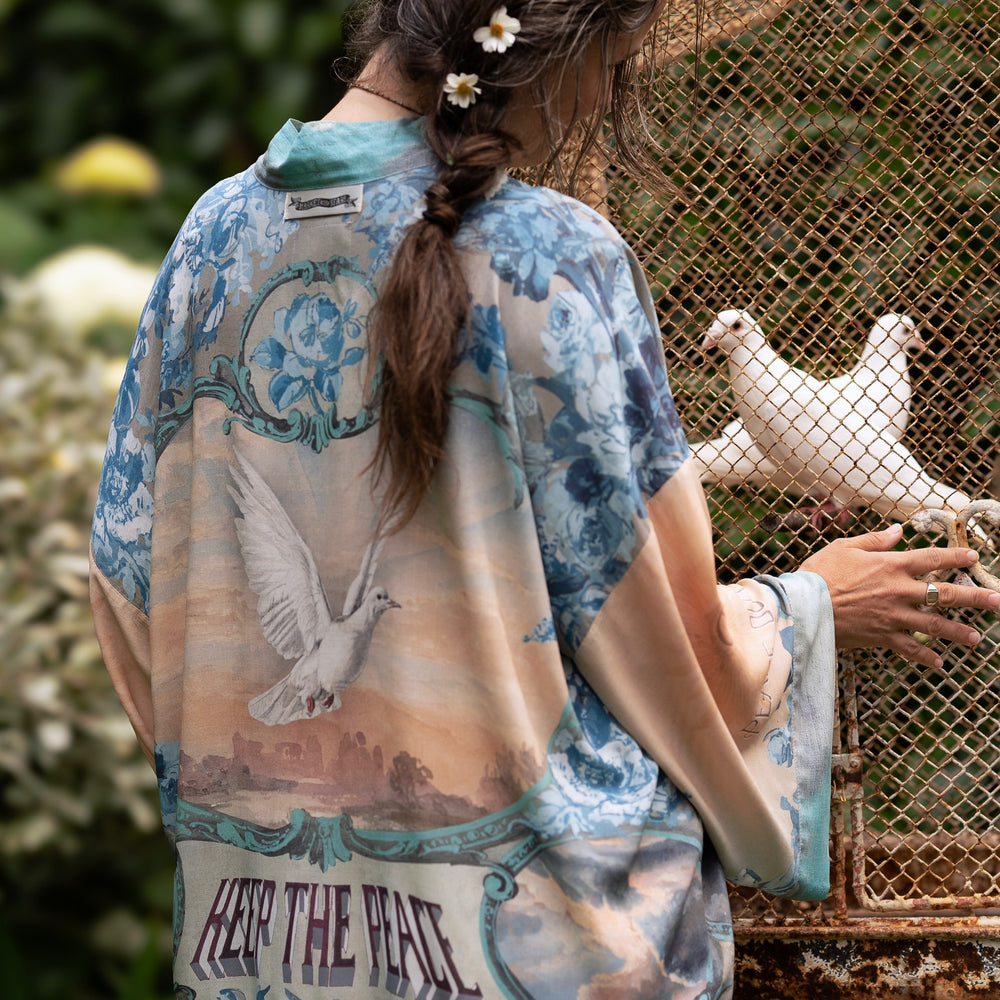 
                  
                    Model wearing our Peace Out Pixie Duster featuring 1800's perfumeur sign with gentle tones of blue & aqua, landscapes, clouds, dove and peace symbols -Market of Stars.
                  
                