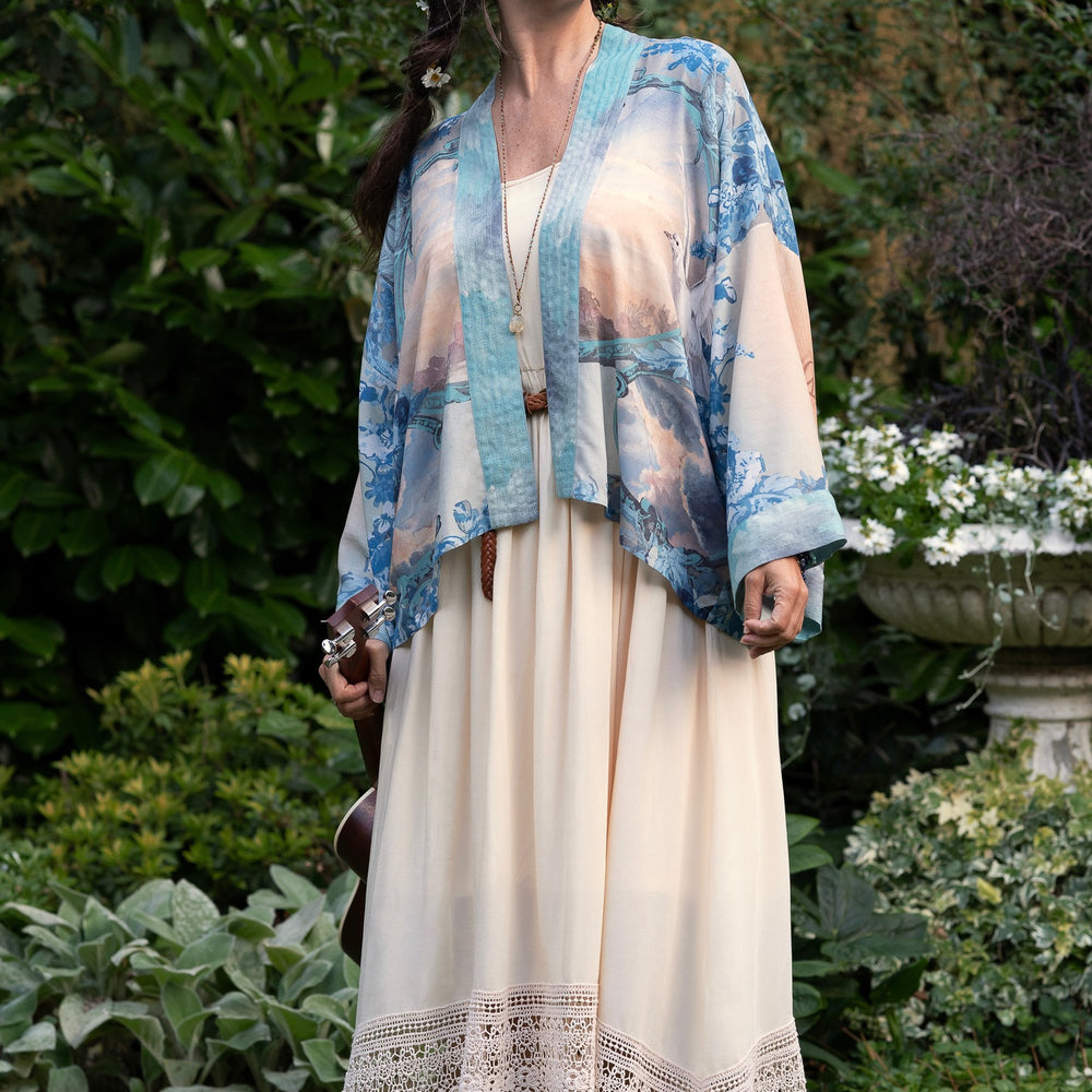 
                  
                    Model wearing our Peace Out Pixie Duster featuring 1800's perfumeur sign with gentle tones of blue & aqua, landscapes, clouds, dove and peace symbols -Market of Stars.
                  
                