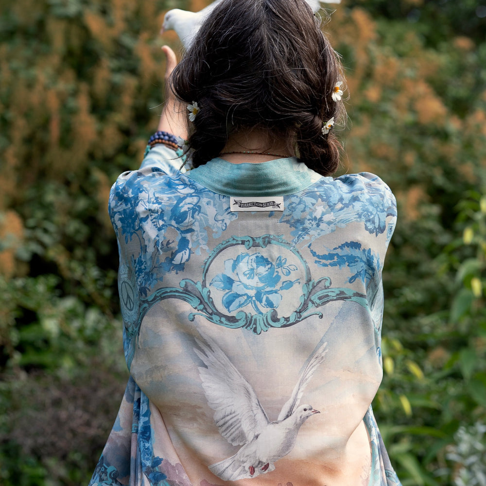 
                  
                    Model wearing our Peace Out Pixie Duster featuring 1800's perfumeur sign with gentle tones of blue & aqua, landscapes, clouds, dove and peace symbols -Market of Stars.
                  
                