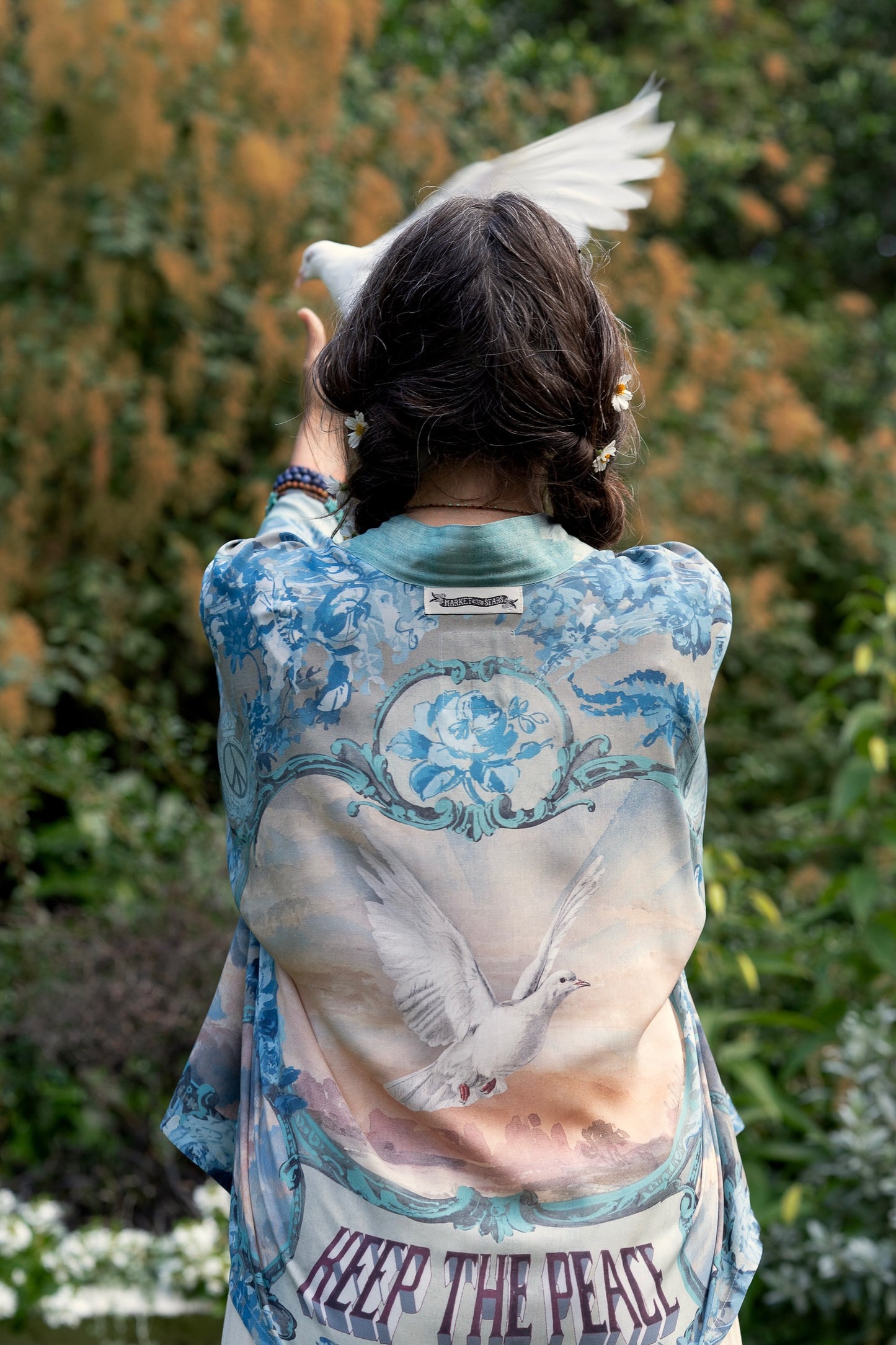 Model wearing our Peace Out Pixie Duster featuring 1800's perfumeur sign with gentle tones of blue & aqua, landscapes, clouds, dove and peace symbols -Market of Stars.
