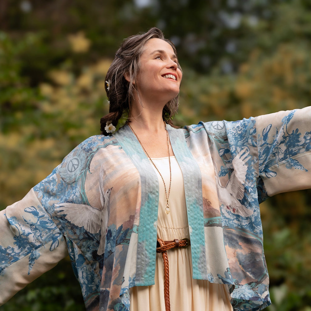
                  
                    Model wearing our Peace Out Pixie Duster featuring 1800's perfumeur sign with gentle tones of blue & aqua, landscapes, clouds, dove and peace symbols -Market of Stars.
                  
                