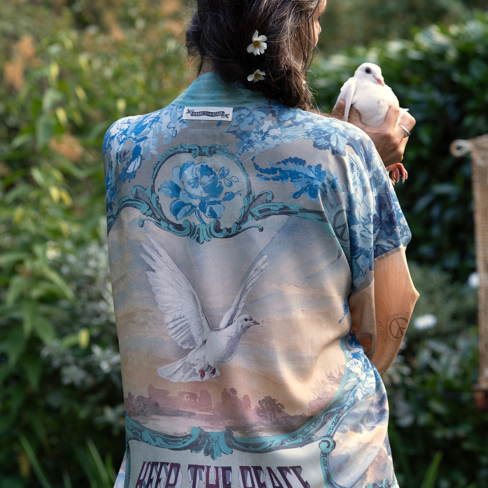
                  
                    Model wearing our Peace Out Pixie Duster featuring 1800's perfumeur sign with gentle tones of blue & aqua, landscapes, clouds, dove and peace symbols -Market of Stars.
                  
                