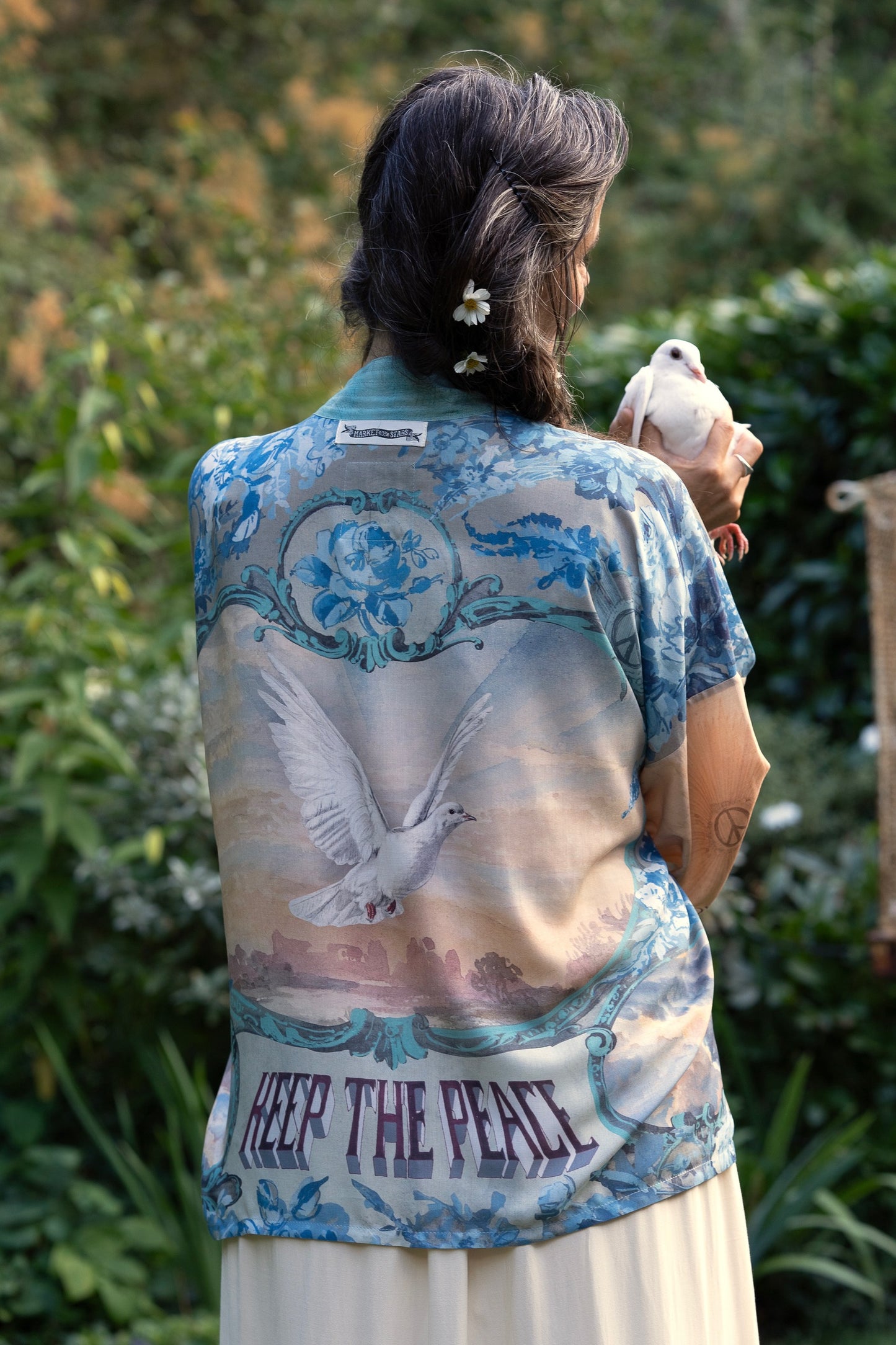 Model wearing our Peace Out Pixie Duster featuring 1800's perfumeur sign with gentle tones of blue & aqua, landscapes, clouds, dove and peace symbols -Market of Stars.