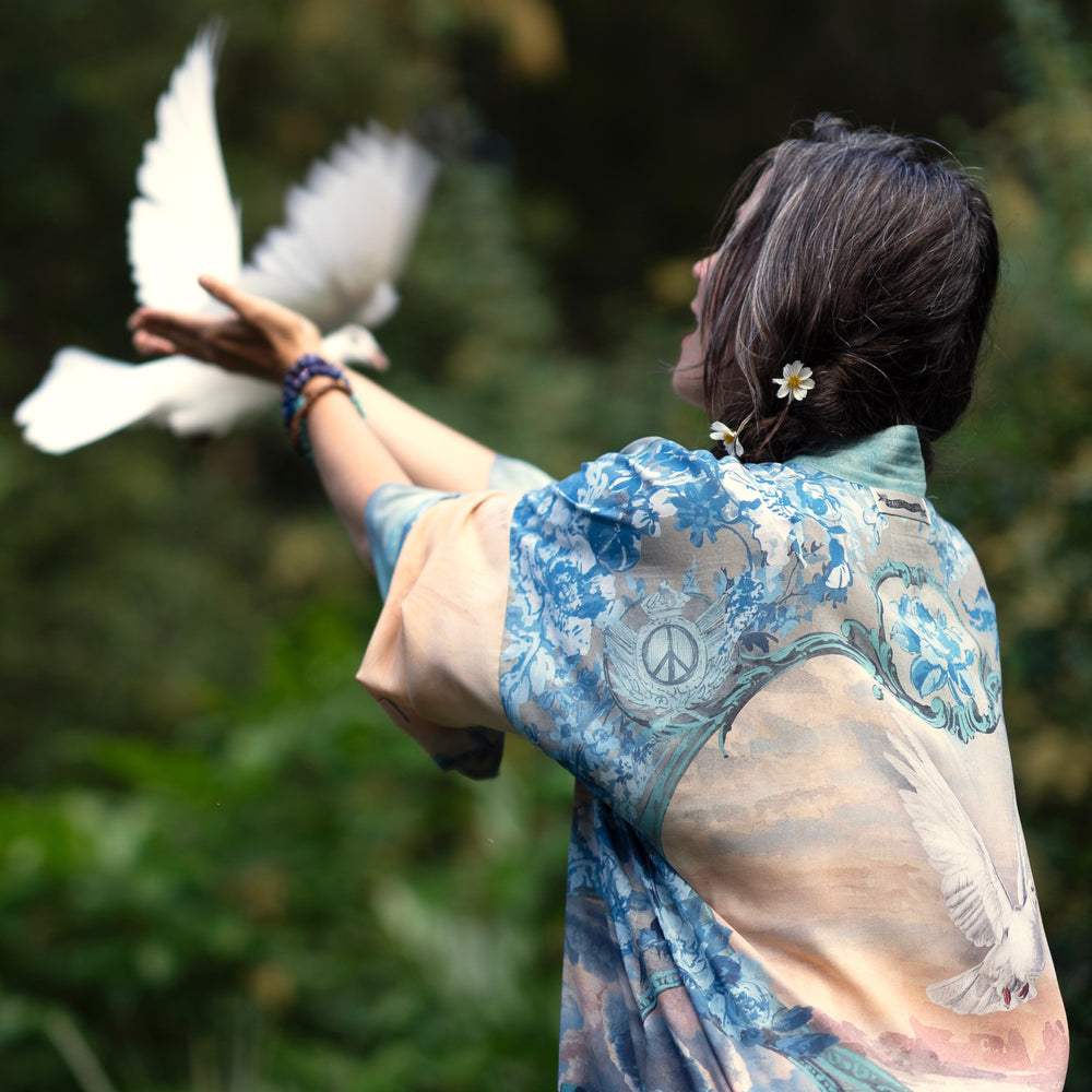 
                  
                    Model wearing our Peace Out Pixie Duster featuring 1800's perfumeur sign with gentle tones of blue & aqua, landscapes, clouds, dove and peace symbols -Market of Stars.
                  
                