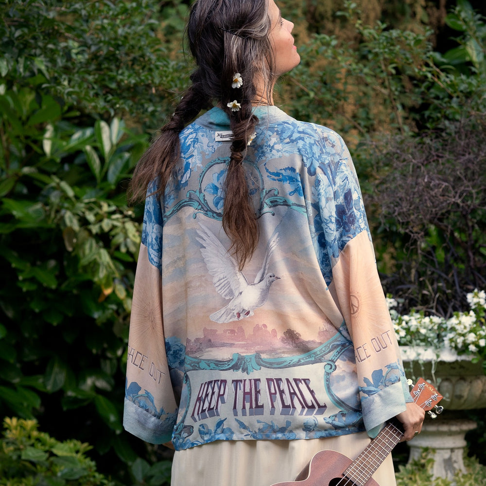 
                  
                    Model wearing our Peace Out Pixie Duster featuring 1800's perfumeur sign with gentle tones of blue & aqua, landscapes, clouds, dove and peace symbols -Market of Stars.
                  
                