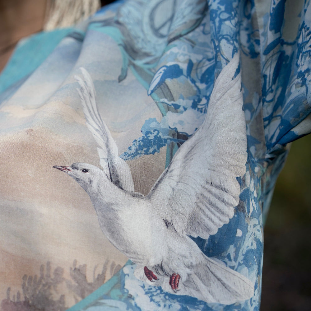 
                  
                    Model wearing our Peace Out Pixie Duster featuring 1800's perfumeur sign with gentle tones of blue & aqua, landscapes, clouds, dove and peace symbols -Market of Stars.
                  
                