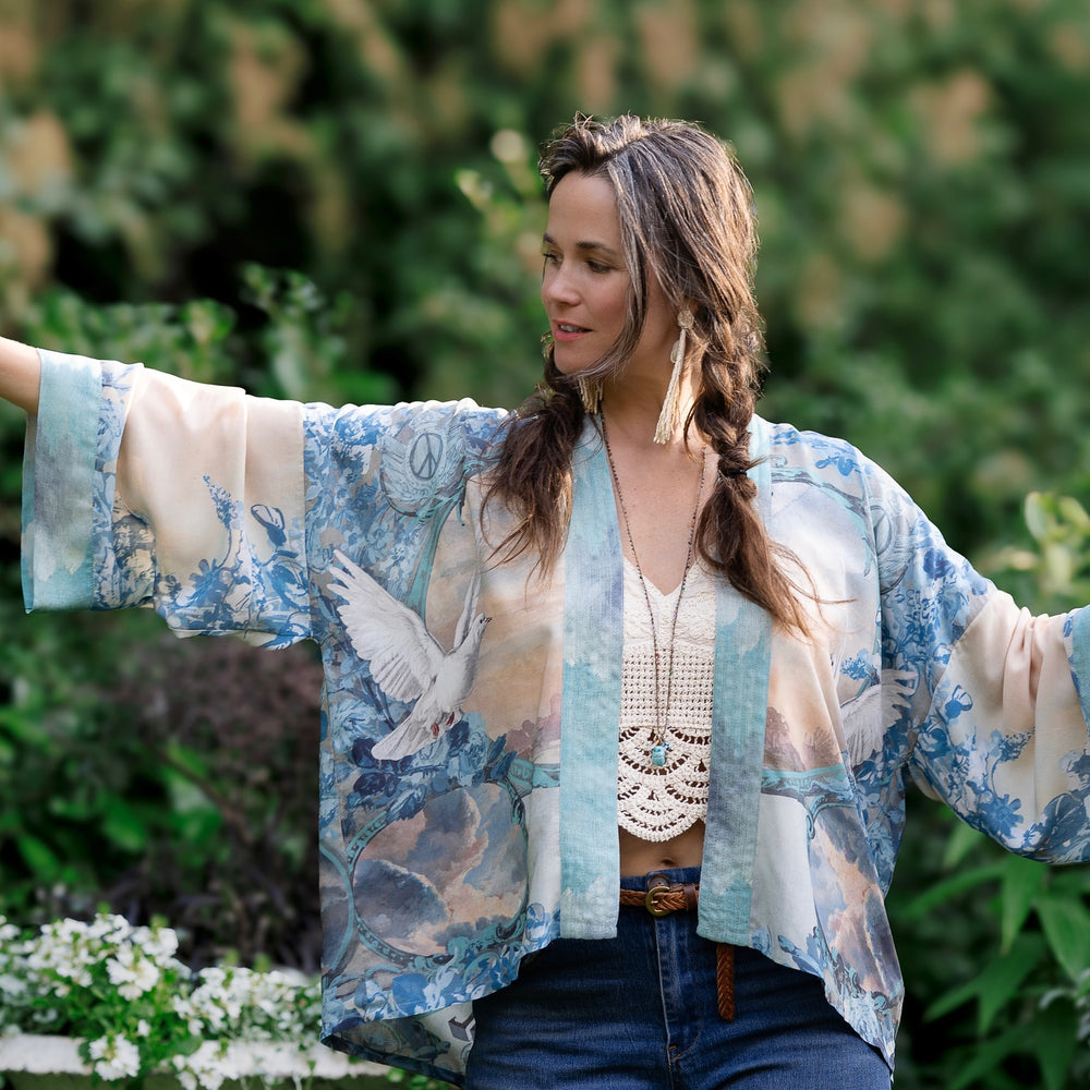 
                  
                    Model wearing our Peace Out Pixie Duster featuring 1800's perfumeur sign with gentle tones of blue & aqua, landscapes, clouds, dove and peace symbols -Market of Stars.
                  
                