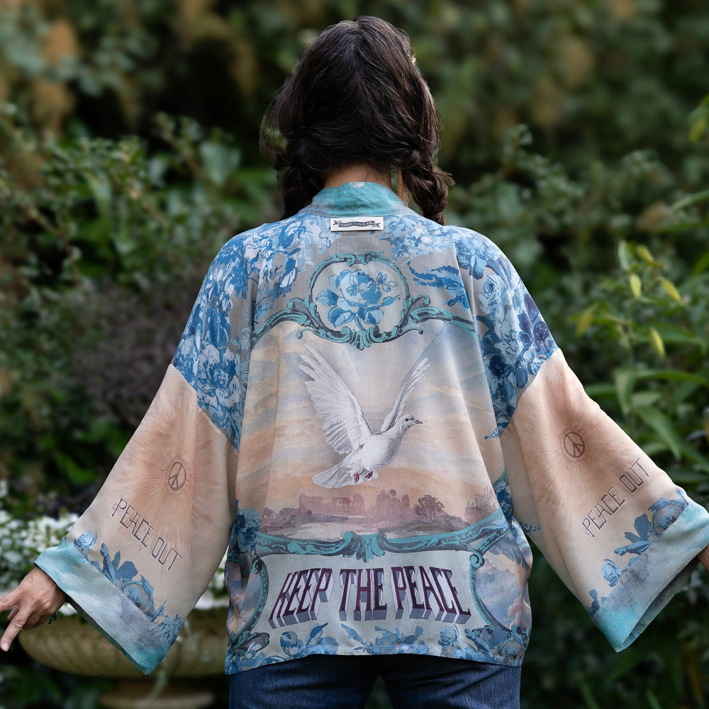 
                  
                    Model wearing our Peace Out Pixie Duster featuring 1800's perfumeur sign with gentle tones of blue & aqua, landscapes, clouds, dove and peace symbols -Market of Stars.
                  
                