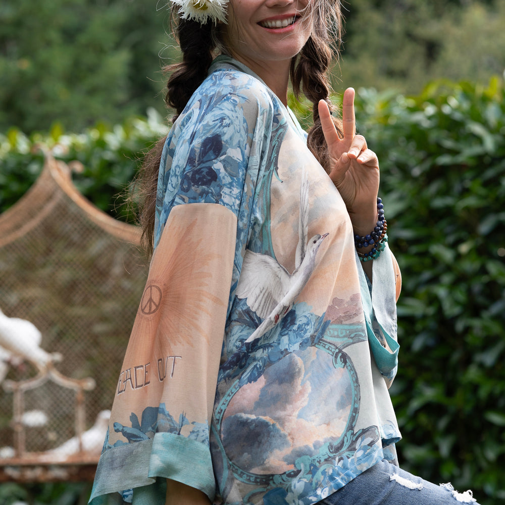 
                  
                    Model wearing our Peace Out Pixie Duster featuring 1800's perfumeur sign with gentle tones of blue & aqua, landscapes, clouds, dove and peace symbols -Market of Stars.
                  
                