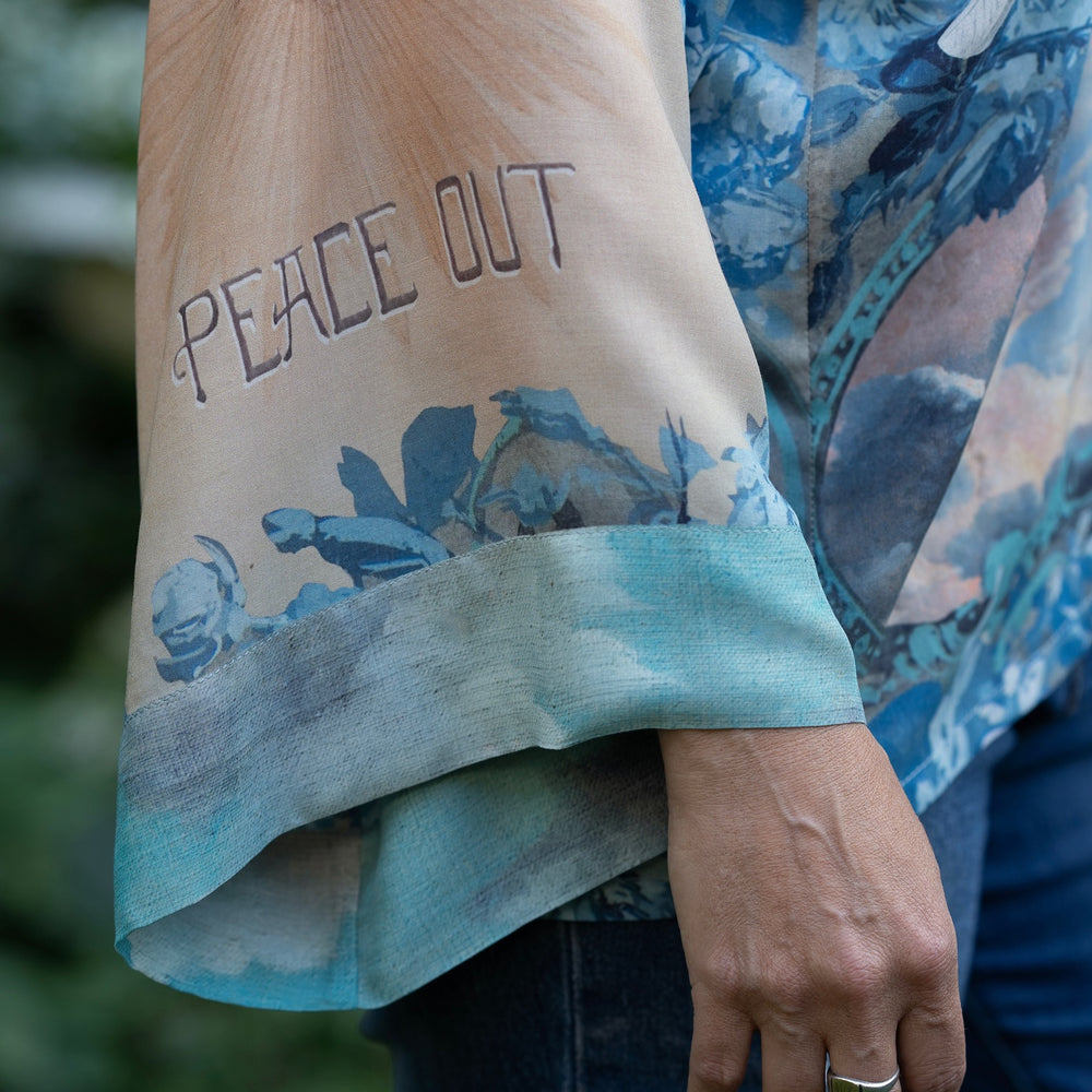 
                  
                    Model wearing our Peace Out Pixie Duster featuring 1800's perfumeur sign with gentle tones of blue & aqua, landscapes, clouds, dove and peace symbols -Market of Stars.
                  
                