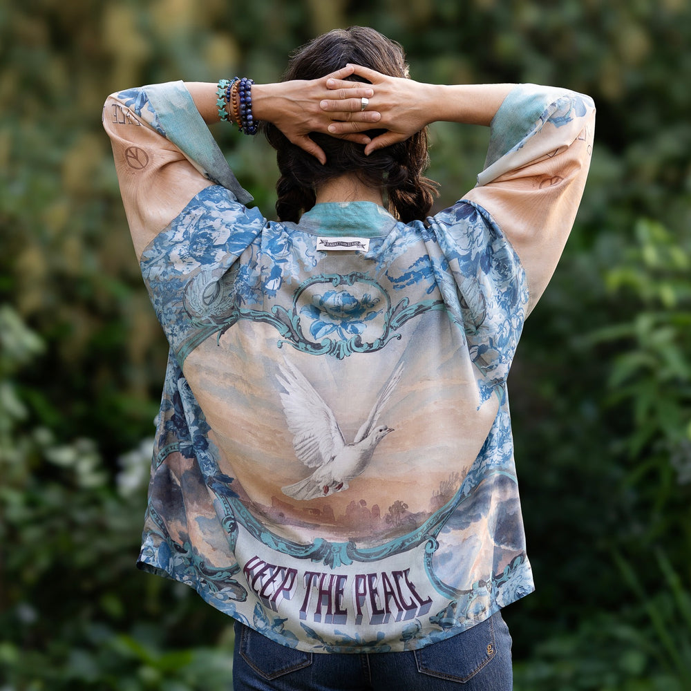 
                  
                    Model wearing our Peace Out Pixie Duster featuring 1800's perfumeur sign with gentle tones of blue & aqua, landscapes, clouds, dove and peace symbols -Market of Stars.
                  
                