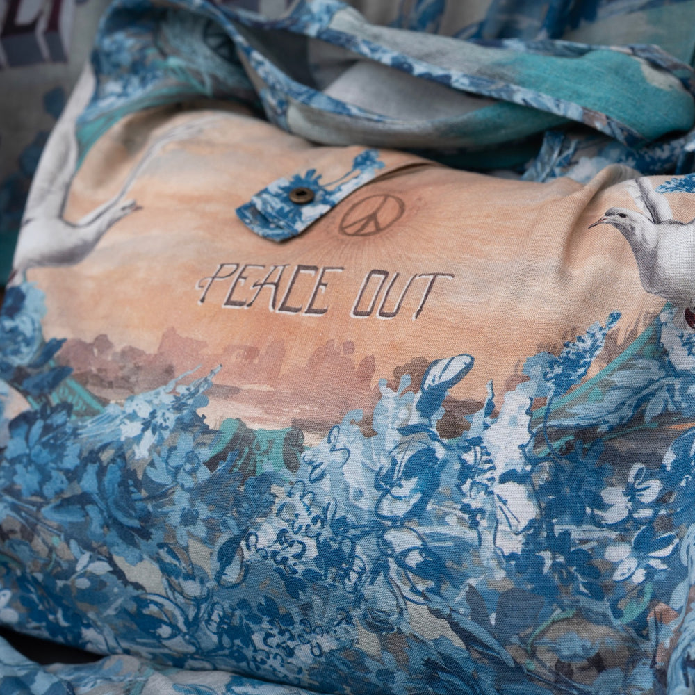 
                  
                    Model wearing our Peace Out tote bag featuring 1800's perfumeur sign with gentle tones of blue & aqua, landscapes, clouds, dove, and peace symbols -Market of Stars.
                  
                