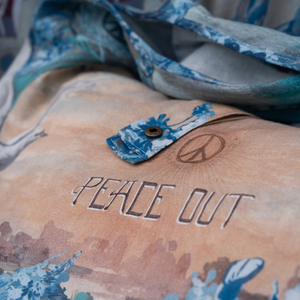 
                  
                    Model wearing our Peace Out tote bag featuring 1800's perfumeur sign with gentle tones of blue & aqua, landscapes, clouds, dove, and peace symbols -Market of Stars.
                  
                