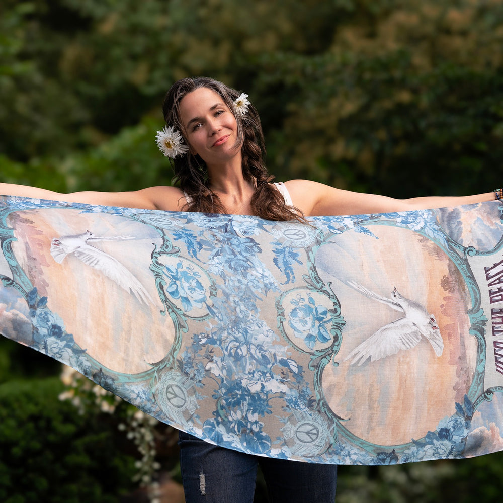 
                  
                    Model wearing our Peace Out scarf featuring 1800's perfumeur sign with gentle tones of blue & aqua, landscapes, clouds, dove, and peace symbols -Market of Stars
                  
                