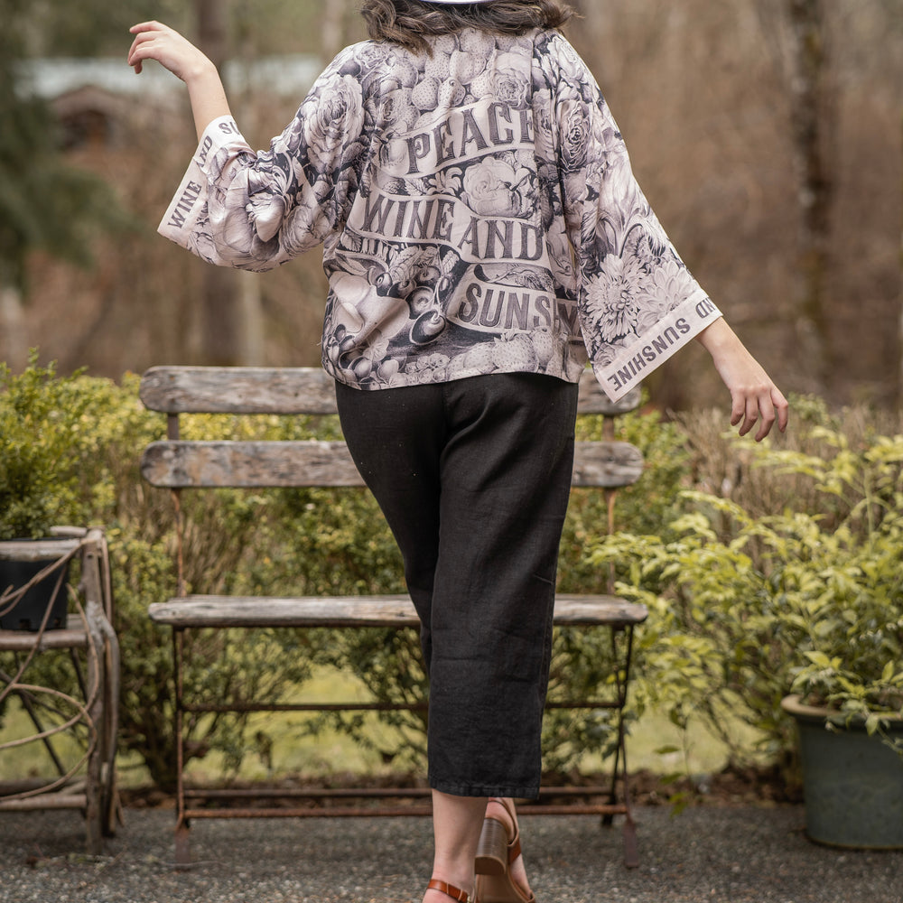 Model wearing Peace, Wine & Sunshine Bohéme Slip Dress featuring botanical collages and playful peace, wine and sunshine lettering on the hem – Market of Stars.