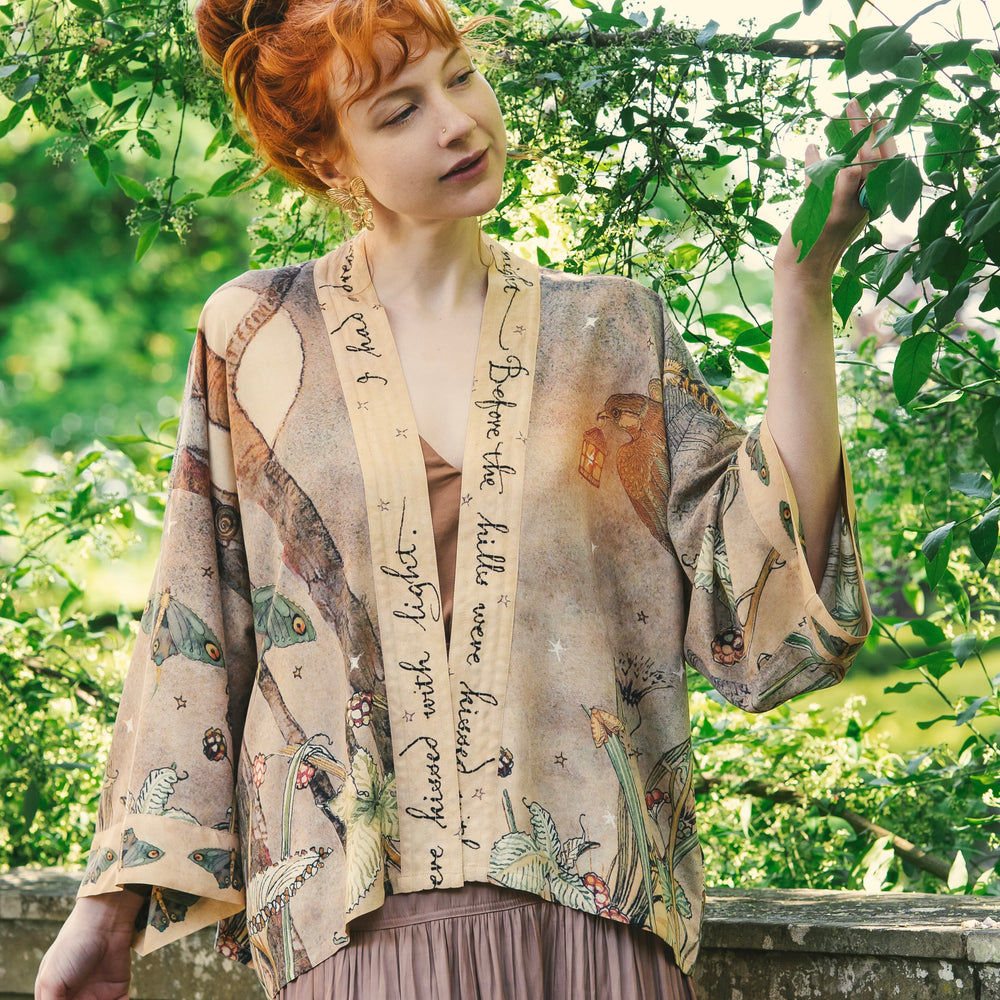 
                  
                    Model wearing an enchanting cropped kimono duster featuring illustrations by Charles van Sandwyck's, crafted from airy bamboo-based viscose with a touch of whimsical magic - Market of Stars
                  
                
