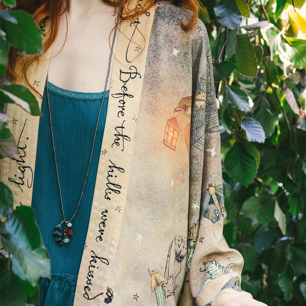 
                  
                    Model wearing an enchanting cropped kimono duster featuring illustrations by Charles van Sandwyck's, crafted from airy bamboo-based viscose with a touch of whimsical magic - Market of Stars
                  
                