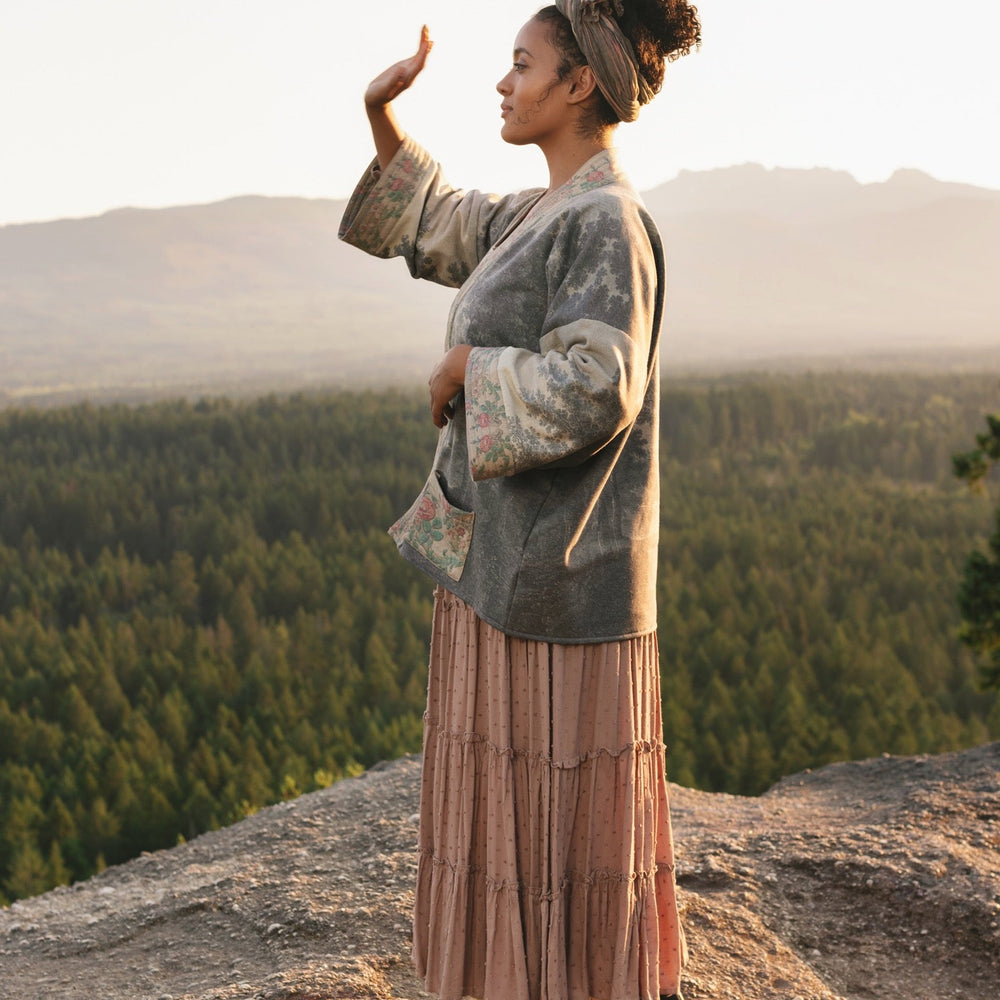 
                  
                    Model wearing the Still I Rise Cottage Cardigan featuring a soft fleece lining and antique landscape etchings in a design inspired by rising strength – Market of Stars
                  
                