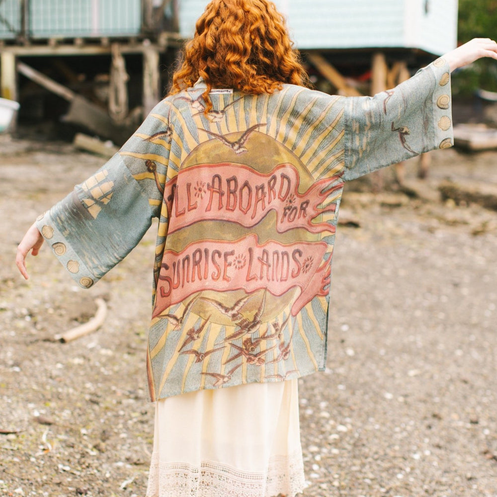 Lightweight duster featuring antique sunrise sky, mermaid, shell, and soaring birds artwork, shown on model at the beach – Market of Stars