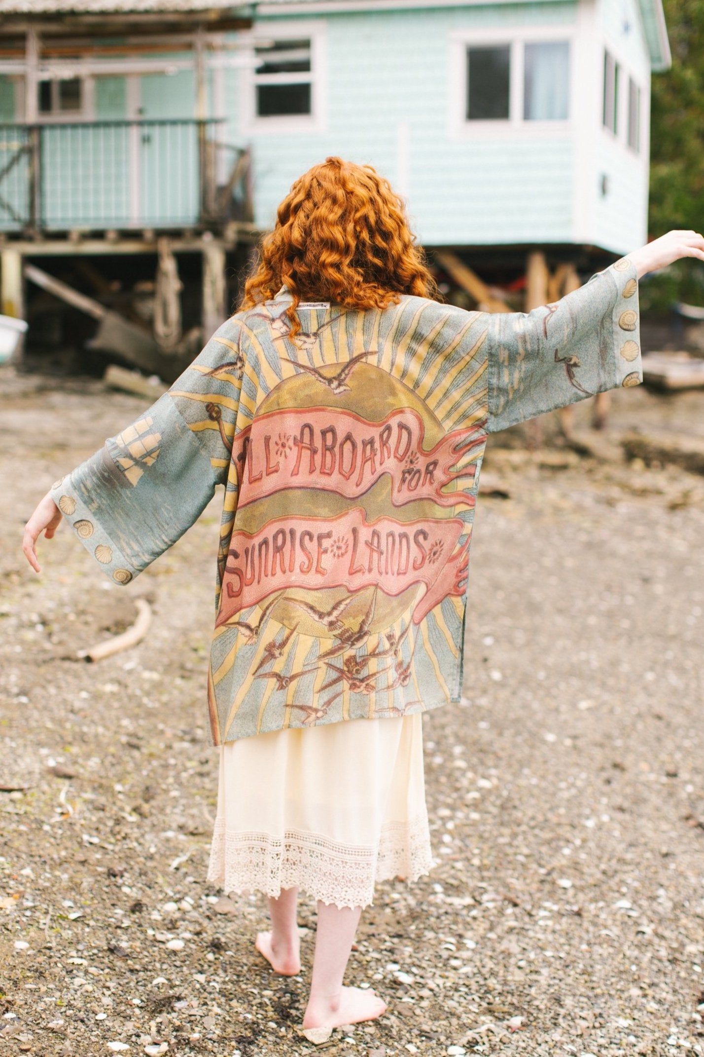 Lightweight duster featuring antique sunrise sky, mermaid, shell, and soaring birds artwork, shown on model at the beach – Market of Stars