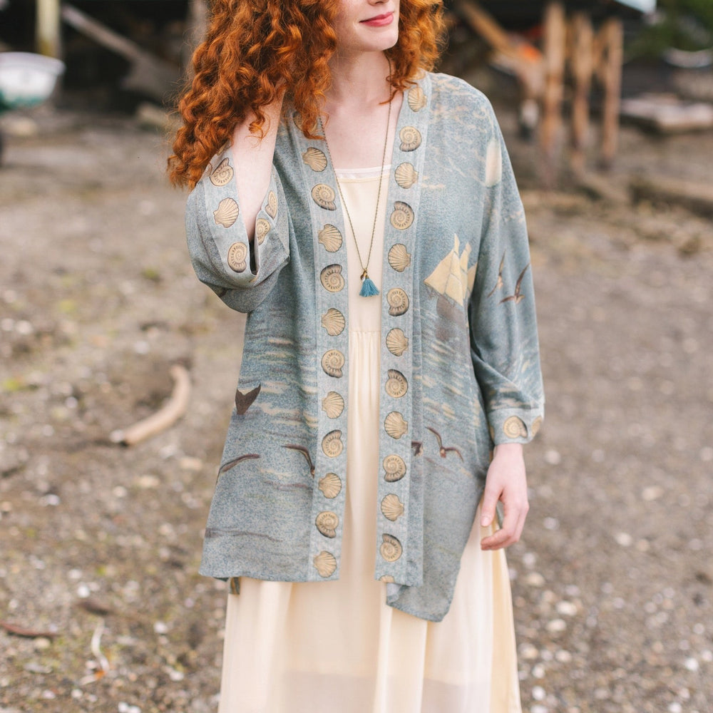 Lightweight duster featuring antique sunrise sky, mermaid, shell, and soaring birds artwork, shown on model at the beach – Market of Stars