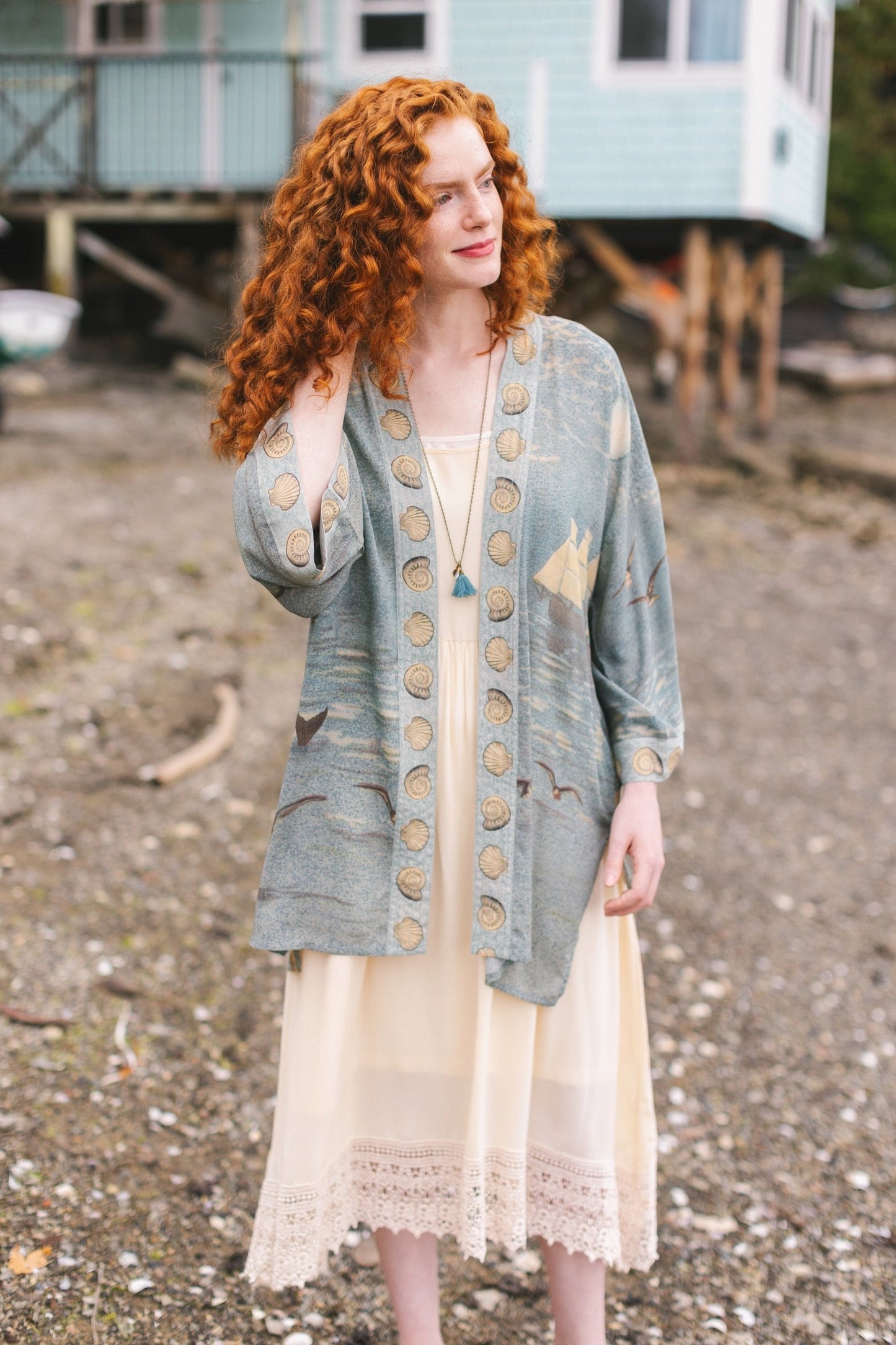 Lightweight duster featuring antique sunrise sky, mermaid, shell, and soaring birds artwork, shown on model at the beach – Market of Stars