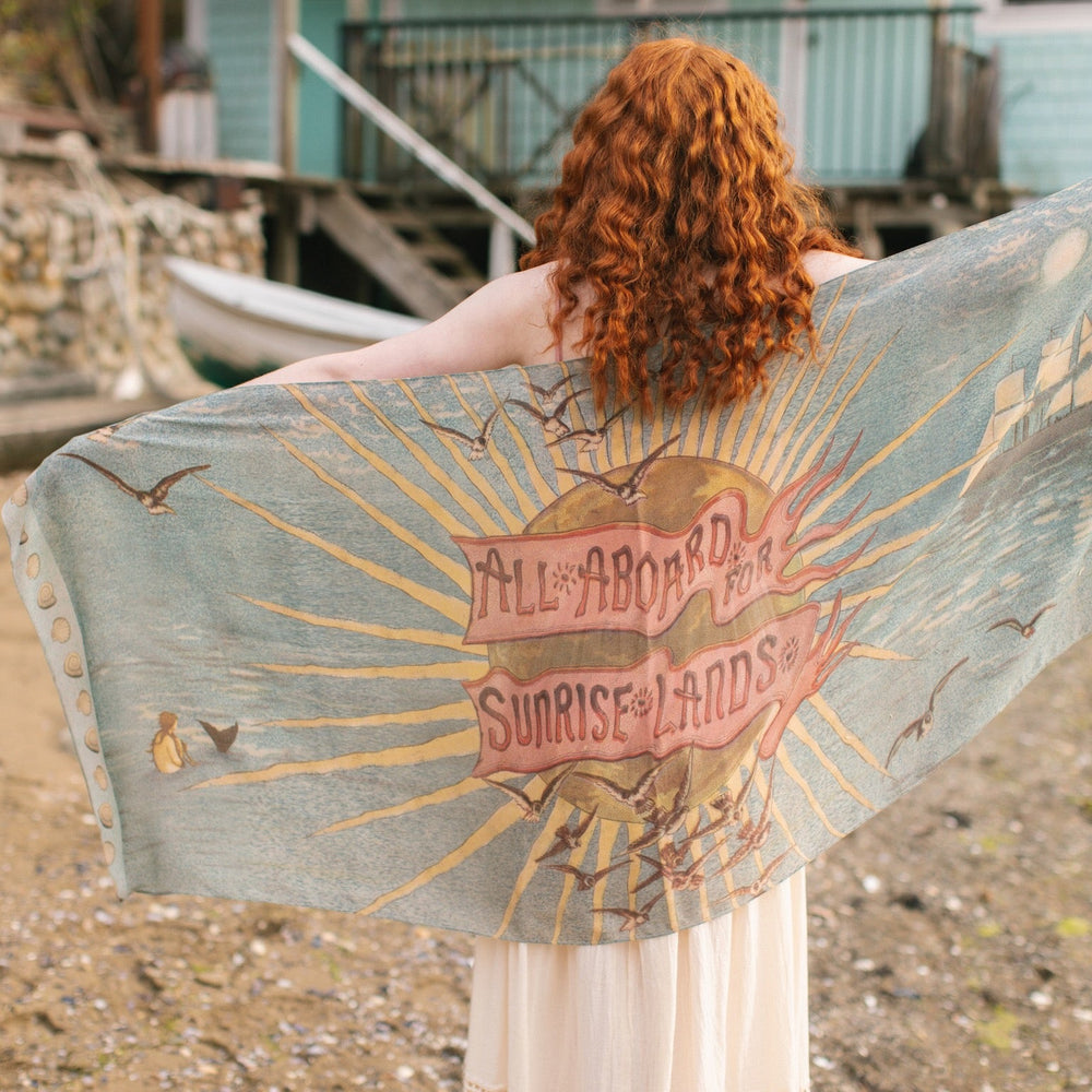 
                  
                    Lightweight scarf featuring a dreamy sunrise landscape and nautical artwork with the words "All aboard for Sunrise Lands" – Market of Stars
                  
                