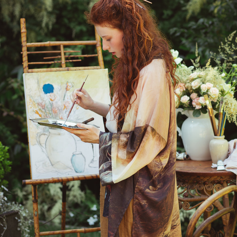 
                  
                    Model wearing The Artist kimono-style duster featuring antique paintings, botanical floral trim, and a radiant golden sun – Market of Stars
                  
                