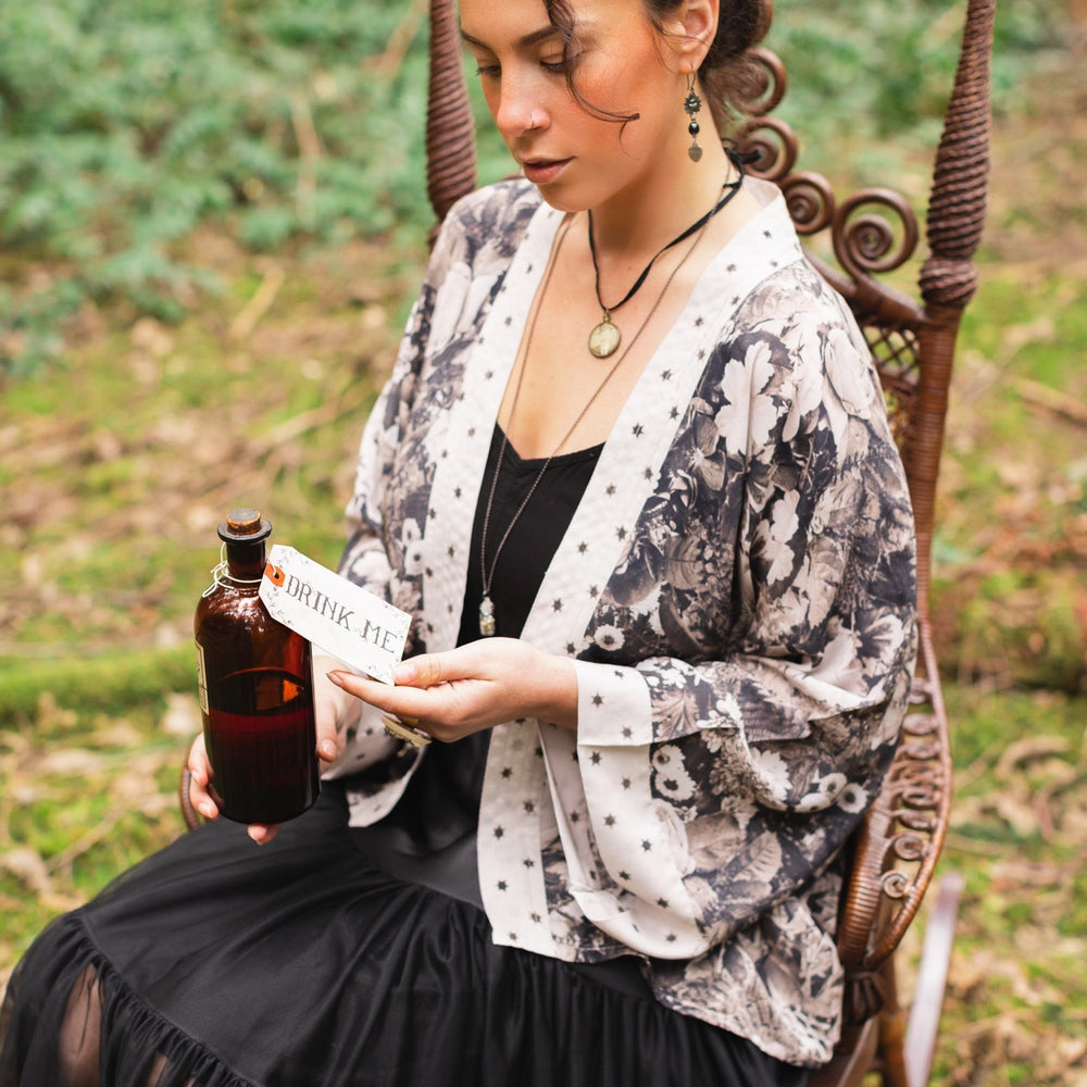 
                  
                    Model wearing Looking Glass Cropped Kimono featuring grown-up Alice Liddell, rare Victorian botanicals, and celestial star and moon accents inspired by Wonderland – Market of Stars.
                  
                