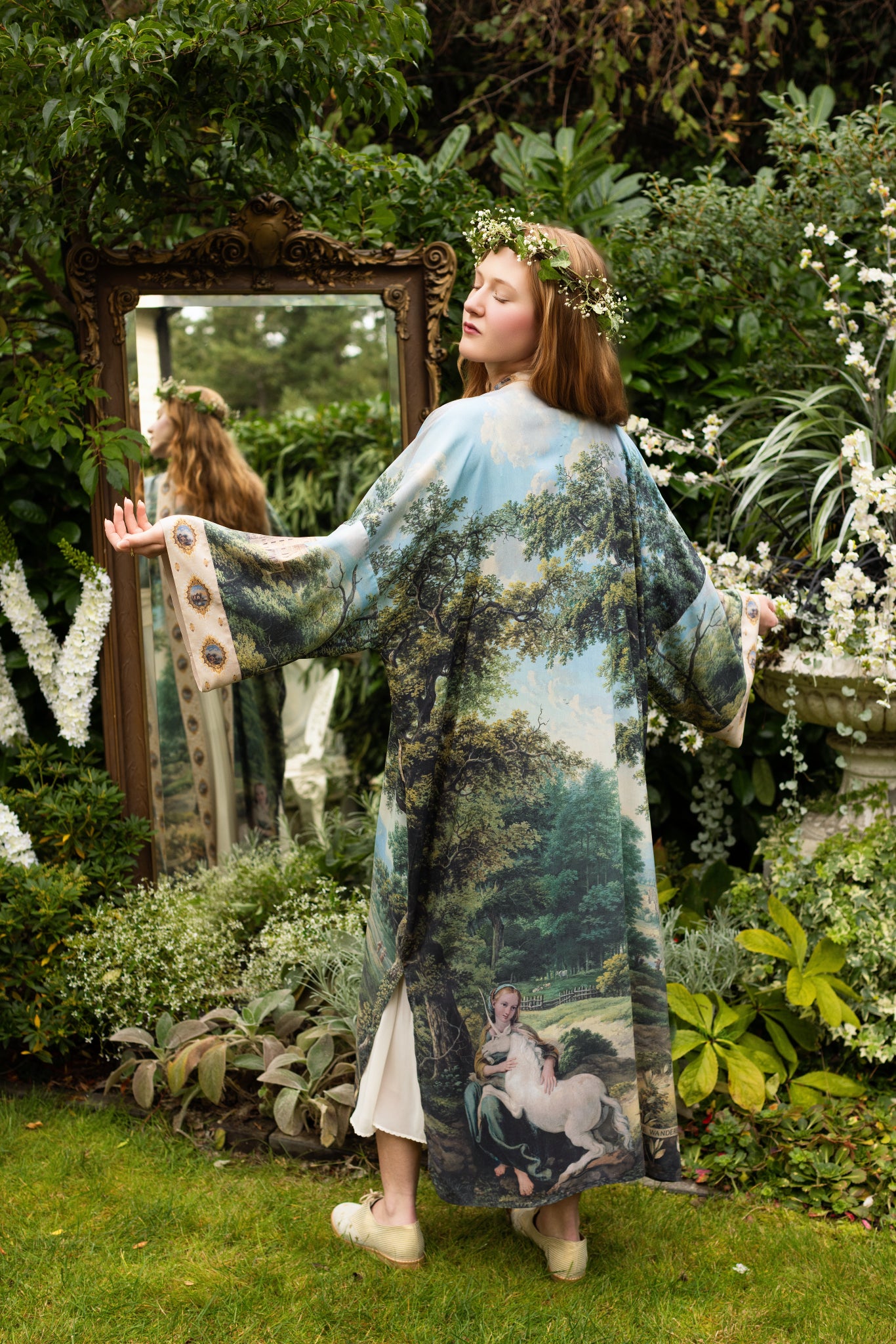 Model wearing a full-length duster ft. vintage artwork & unicorn lorn set against a mossy-green landscape — a romantic piece for the modern dreamer - Market of Stars