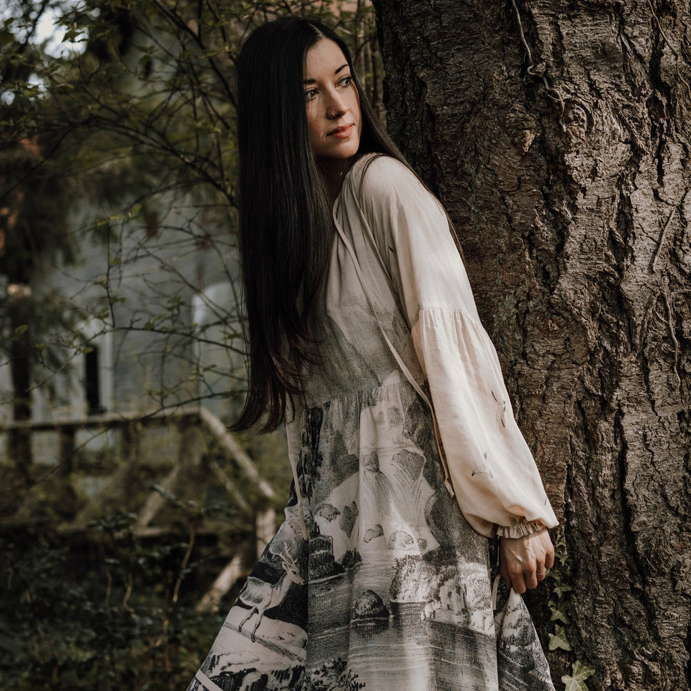 
                  
                    Model wearing knee-length dress with long sleeves featuring vintage print of a forest, songbirds and sunshine - Market of Stars
                  
                
