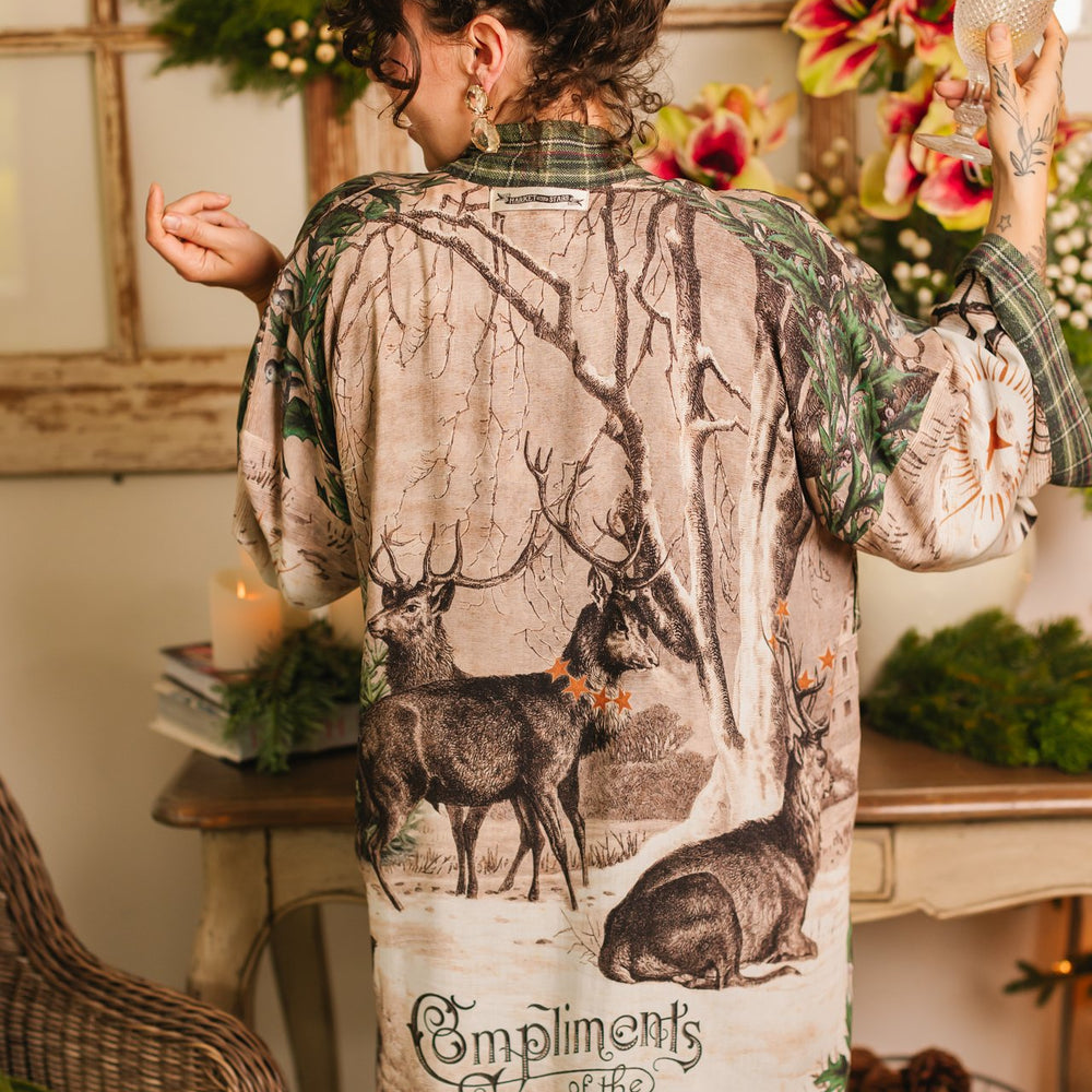 Model wearing a bamboo viscose mid-length duster with Victorian-era images from holiday greeting cards — including reindeer in the snow, a little fir tree, golden stars, and traditional plaid trim - Market of Stars