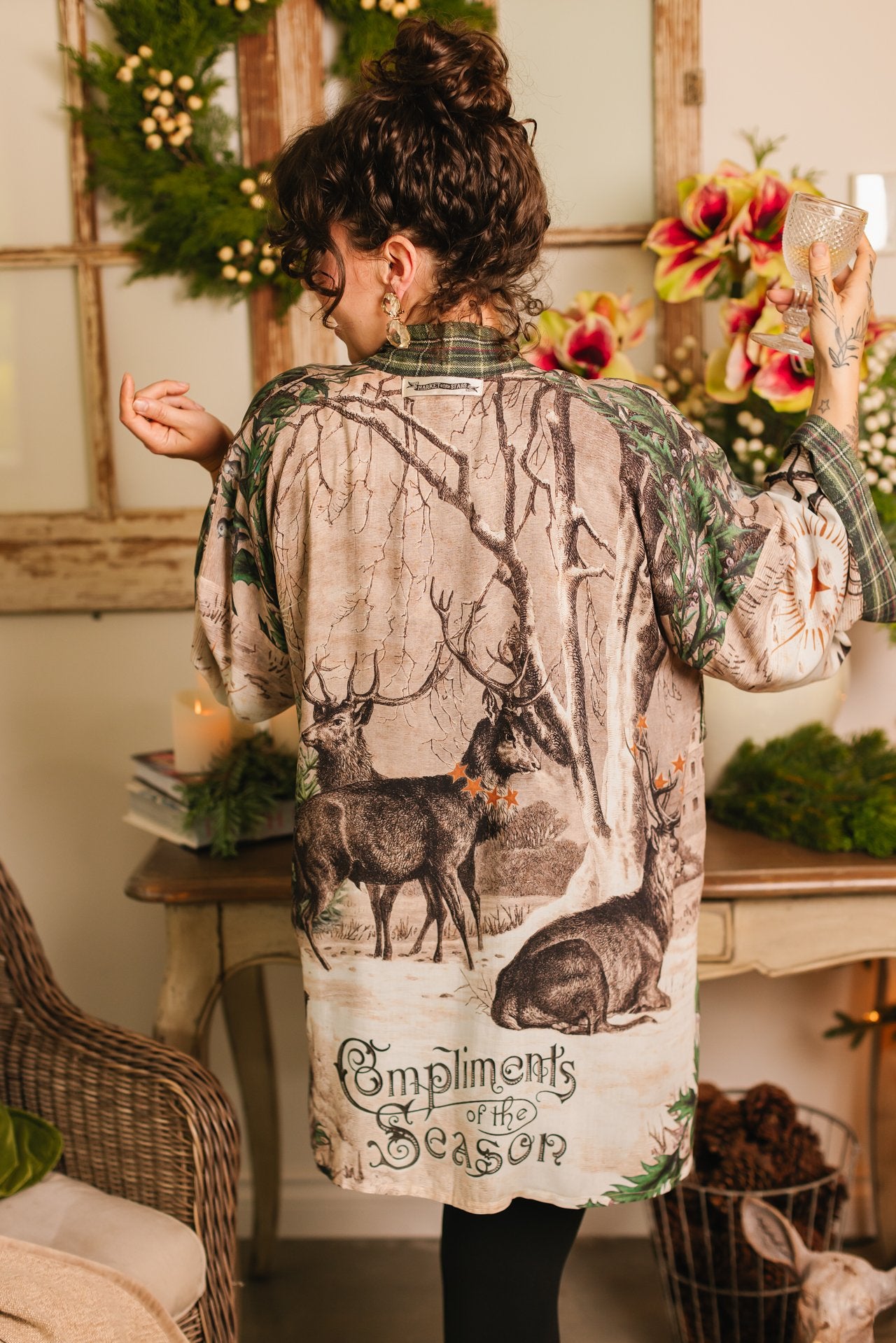 Model wearing a bamboo viscose mid-length duster with Victorian-era images from holiday greeting cards — including reindeer in the snow, a little fir tree, golden stars, and traditional plaid trim - Market of Stars